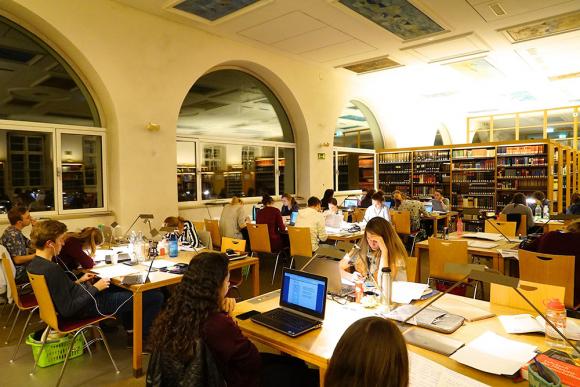 Menschen sitzen an Tischen in einer Universitätsbibliothek