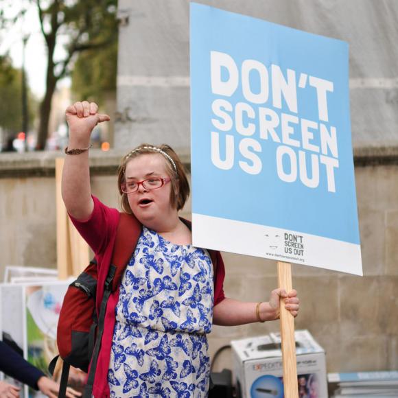 Eine Person hält ein Protestschild mit der Aufschrift "Don't Screen Us Out"