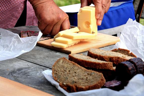 Käse wird geschnitten, im Vordergrund liegt ein geschnittenes Vollkornbrot